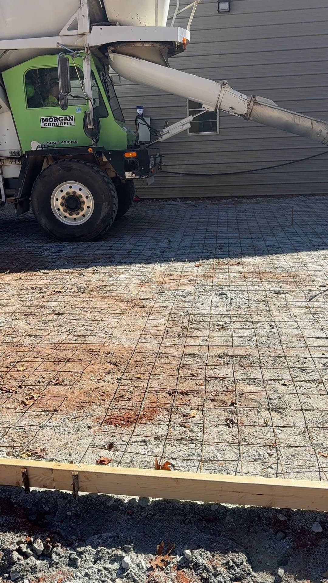 Concrete truck pouring fresh concrete onto rebar grid for foundation construction.