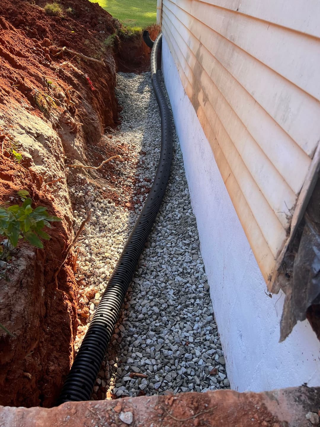 Underground drainage installation beside a house with gravel and black piping in a trench.