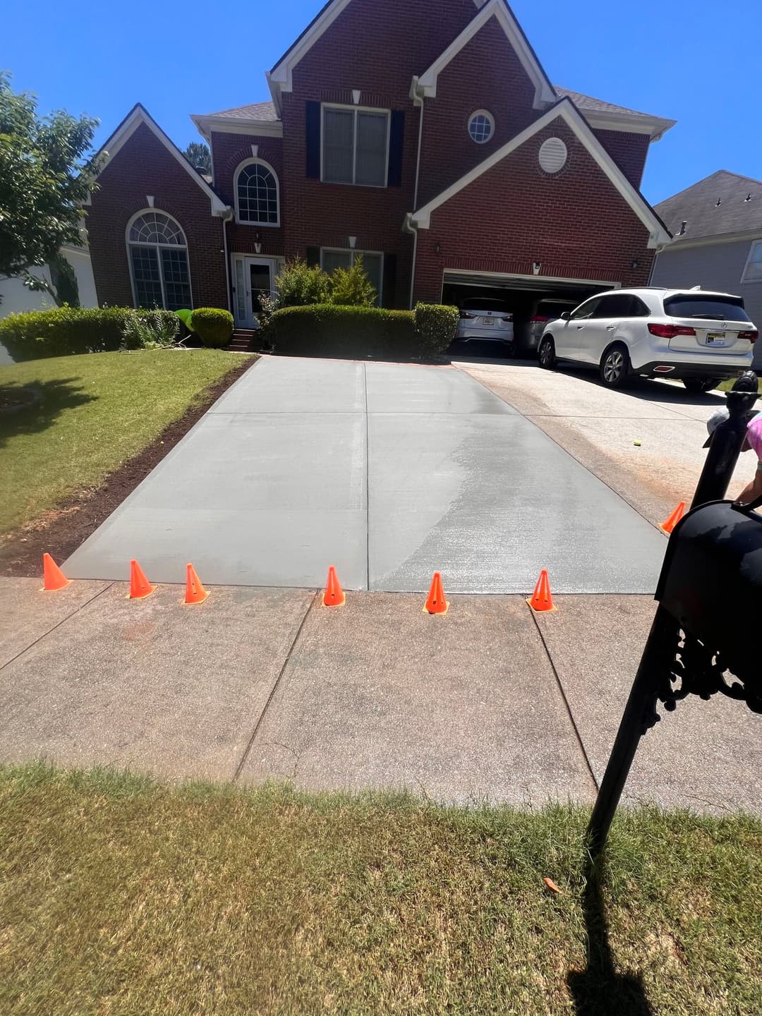 Freshly poured concrete driveway with safety cones, adjacent house and landscaped yard.
