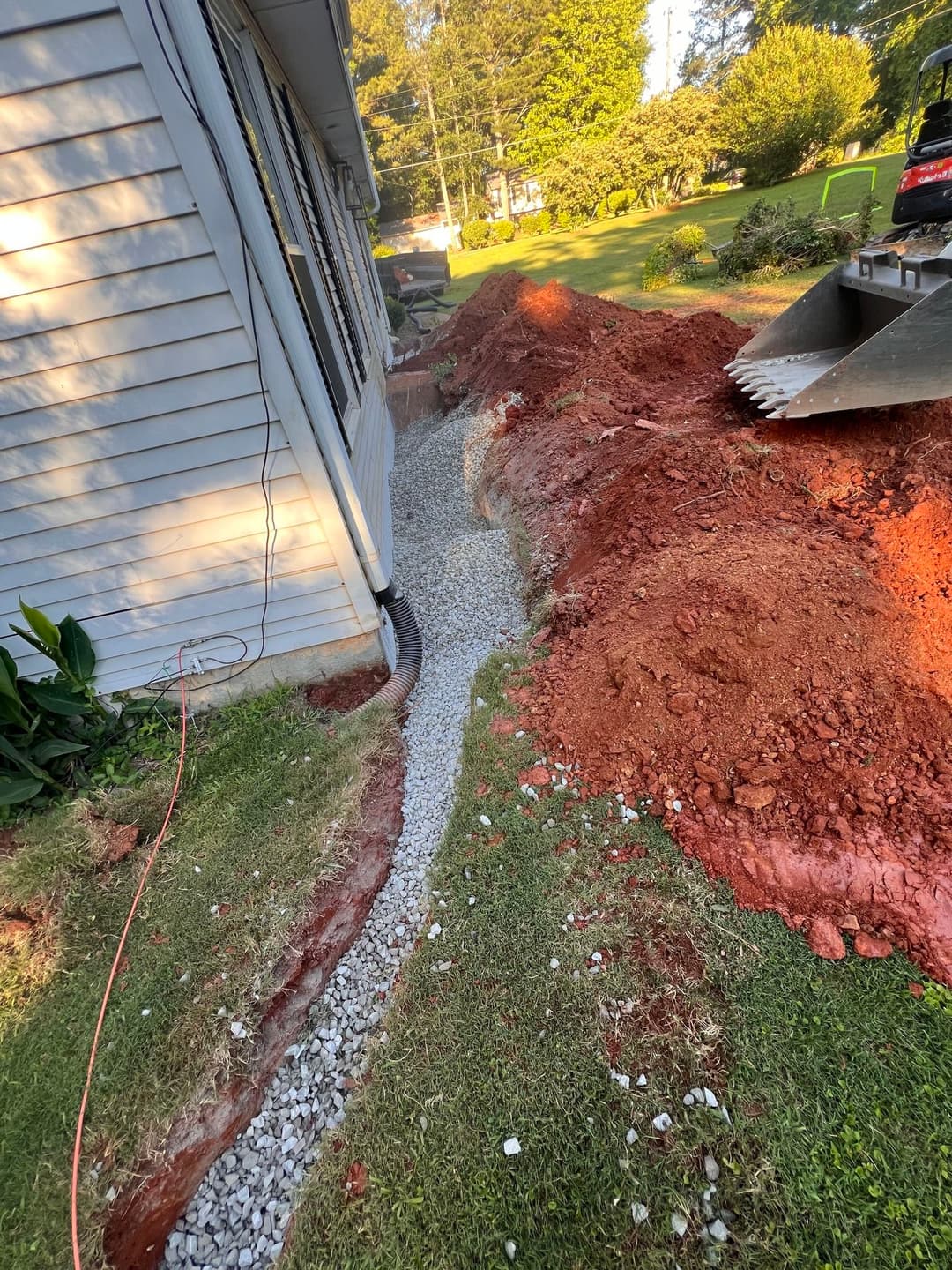 Gravel drainage path alongside a house with excavated soil in the background.