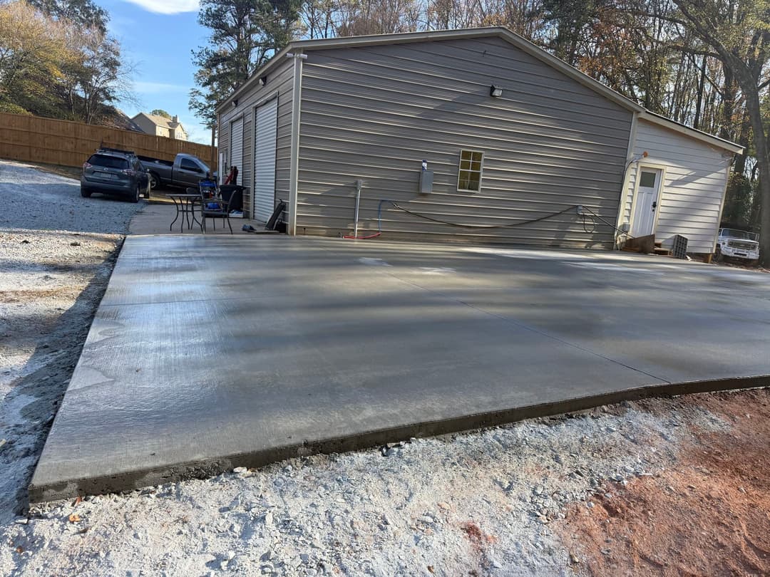 Newly poured concrete slab in front of storage building with parked cars nearby.