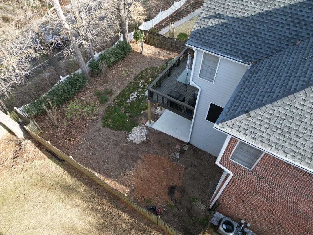Aerial view of a backyard with a patio, garden area, and surrounding trees and fence.